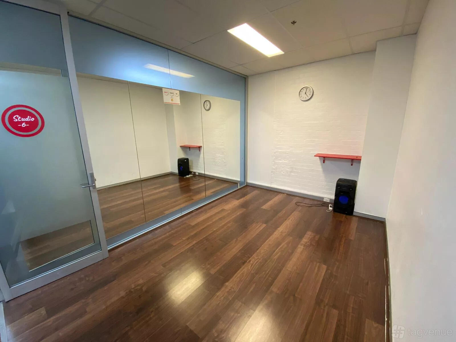 A dance studio with mirrored walls, wooden floors, a wall clock, and a speaker at Latin Dance Australia.