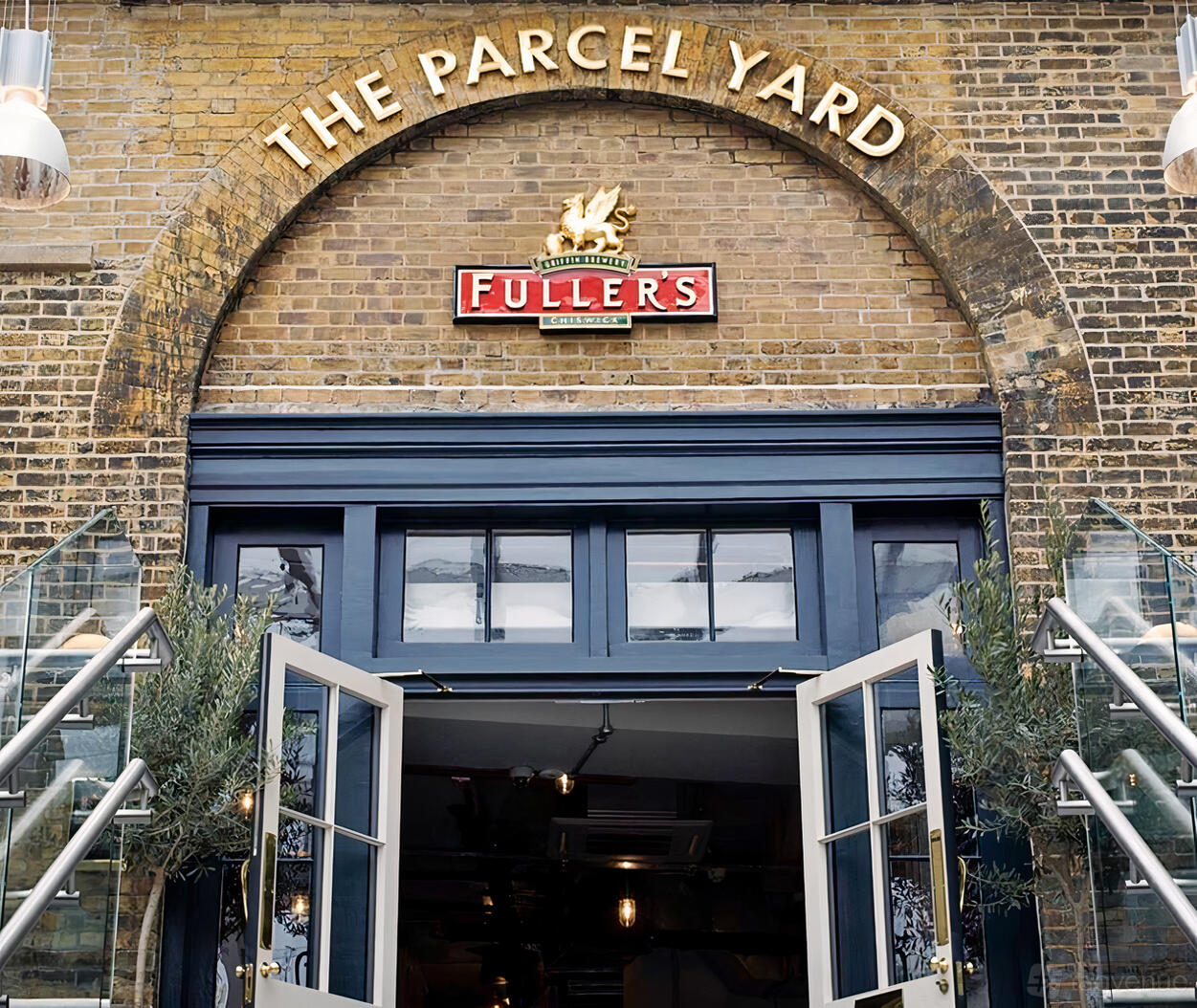 A historic building with arched brick entrance, Fuller's sign, and glass doors at The Parcel Yard.