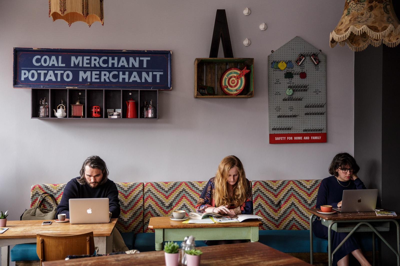 An event space in a cafe with a chevron-patterned bench, vintage signs, and people working at Esquires Coffee Balham.