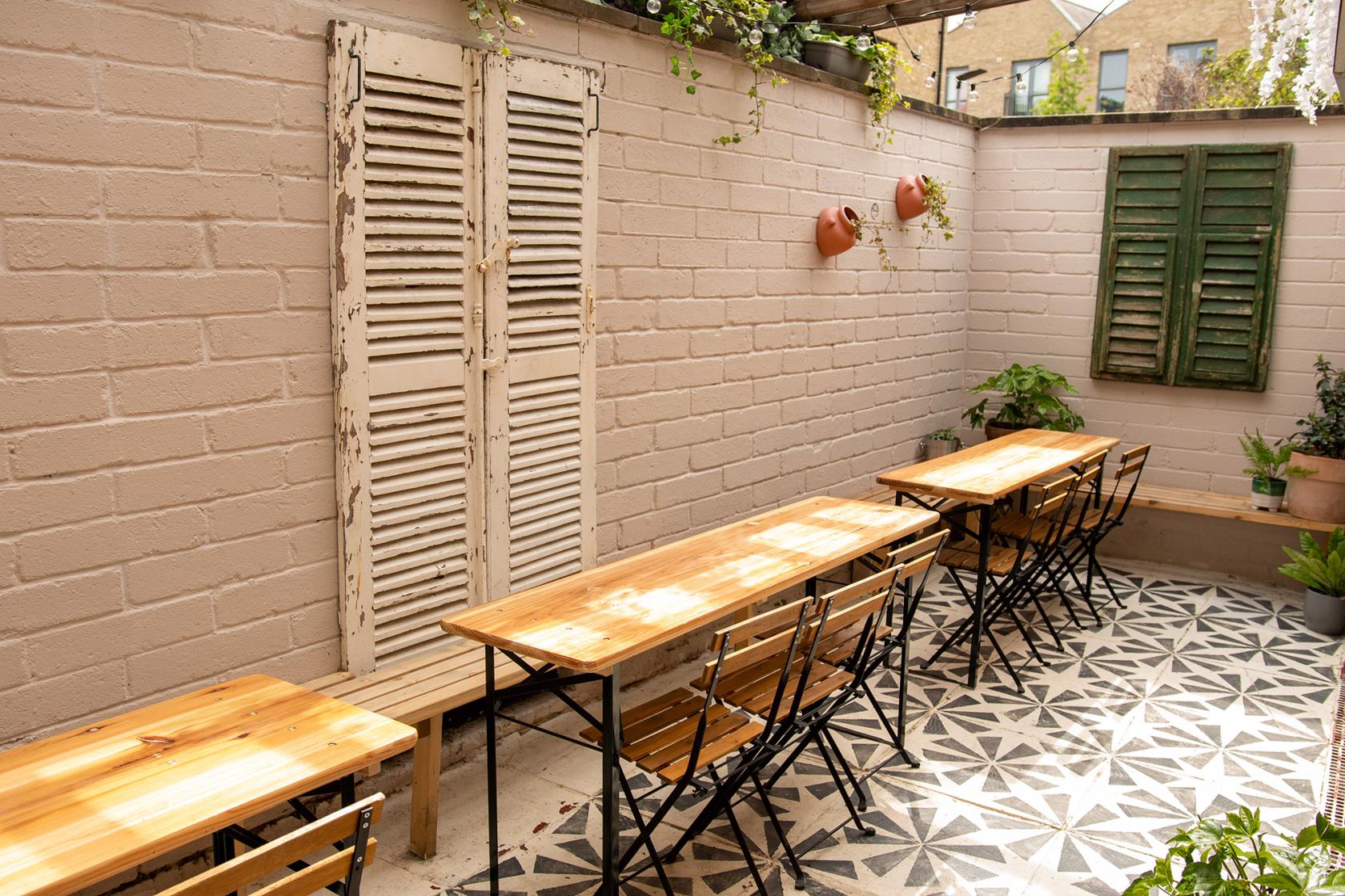 A pub with wooden tables, metal chairs, patterned tile flooring, and potted plants at The Clubhouse at The Vic.