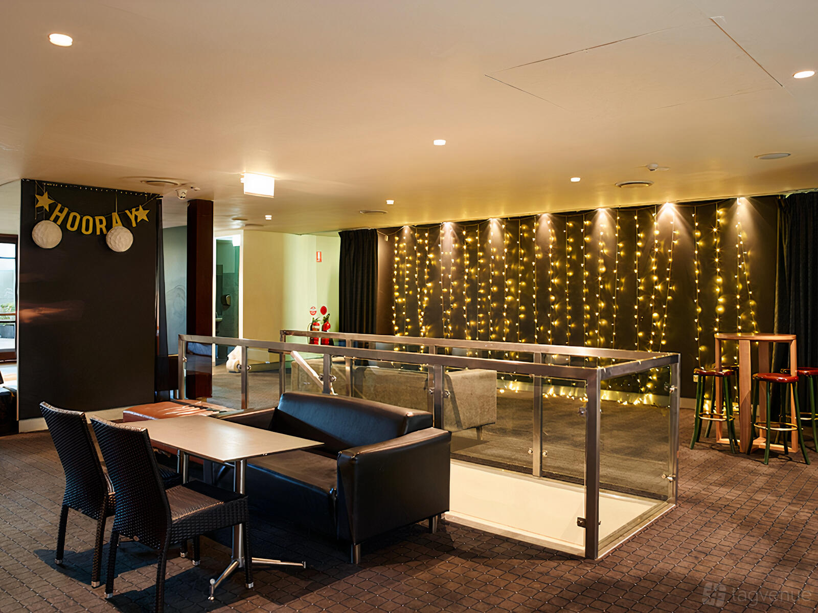 A function room with string lights on a black curtain, lounge seating, and a few high tables at Canley Hotel.