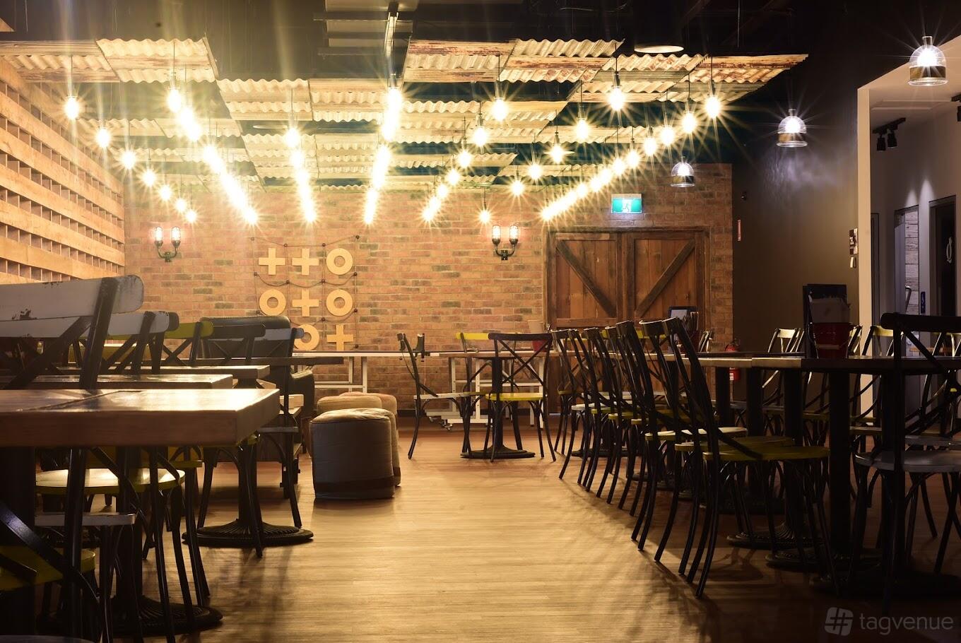 A function room with exposed brick walls, string lights, wooden tables, and chairs at Kingpin North Strathfield.