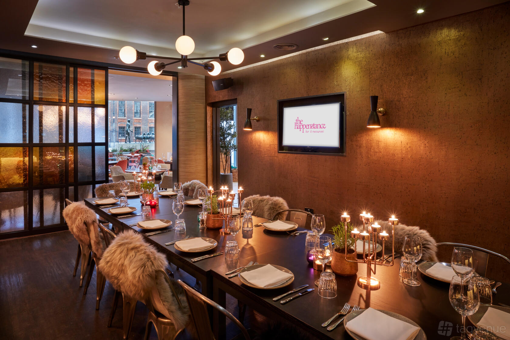 A restaurant dining area with a long wooden table, fur-covered chairs, candlelit centerpieces, and warm lighting at The Happenstance – Paternoster Square.