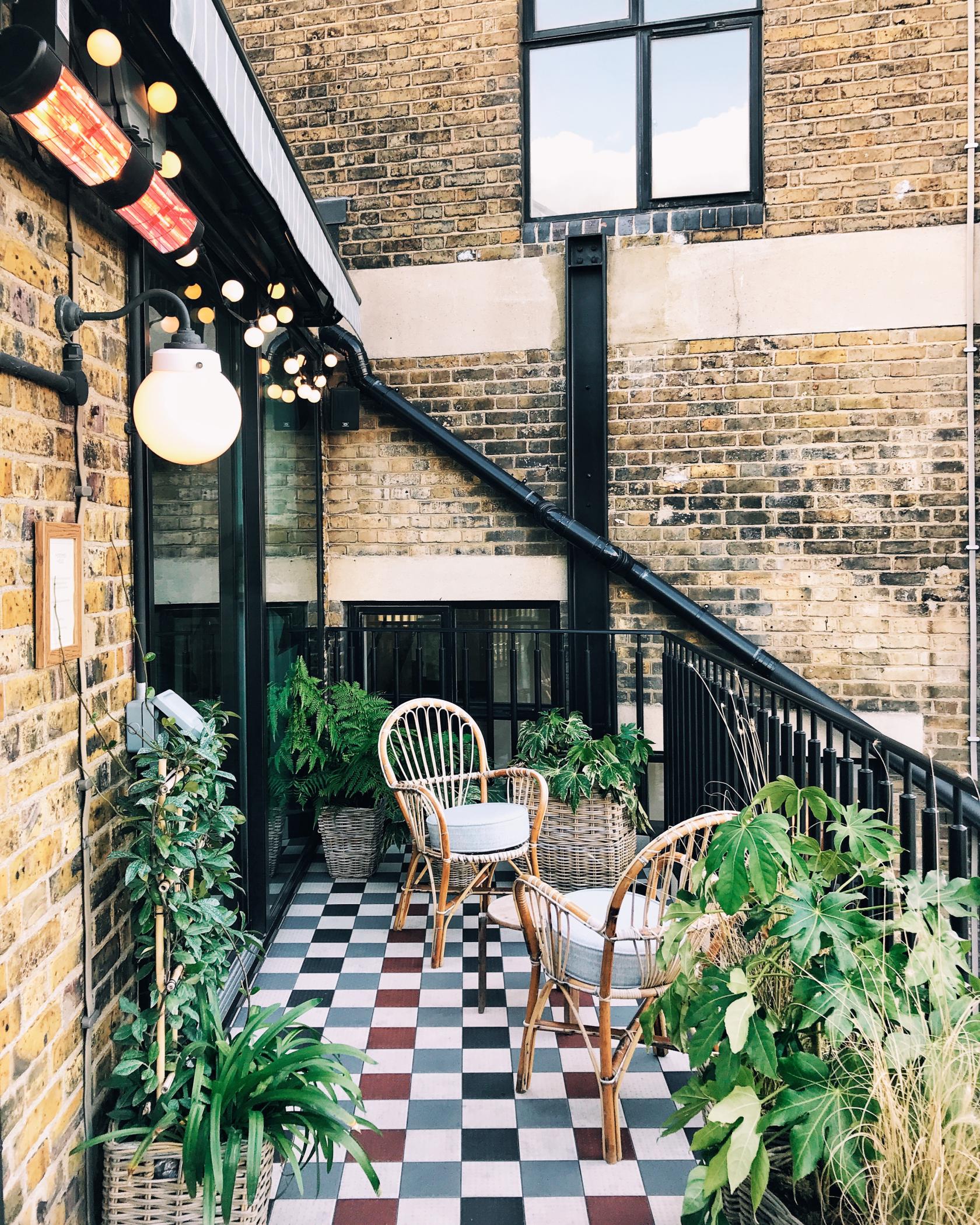 An event space with wicker chairs, potted plants, checkered flooring, and exposed brick walls at Mortimer House.