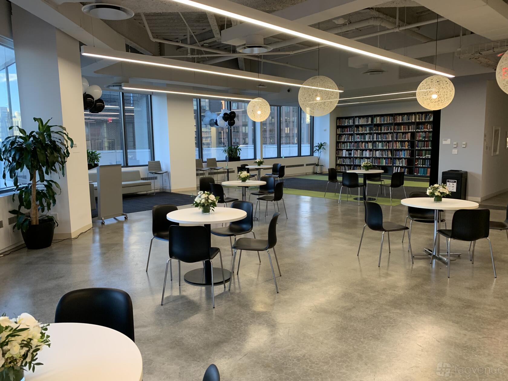 A library in an office space with floor-to-ceiling windows, round tables with chairs, and bookshelves at Candid.