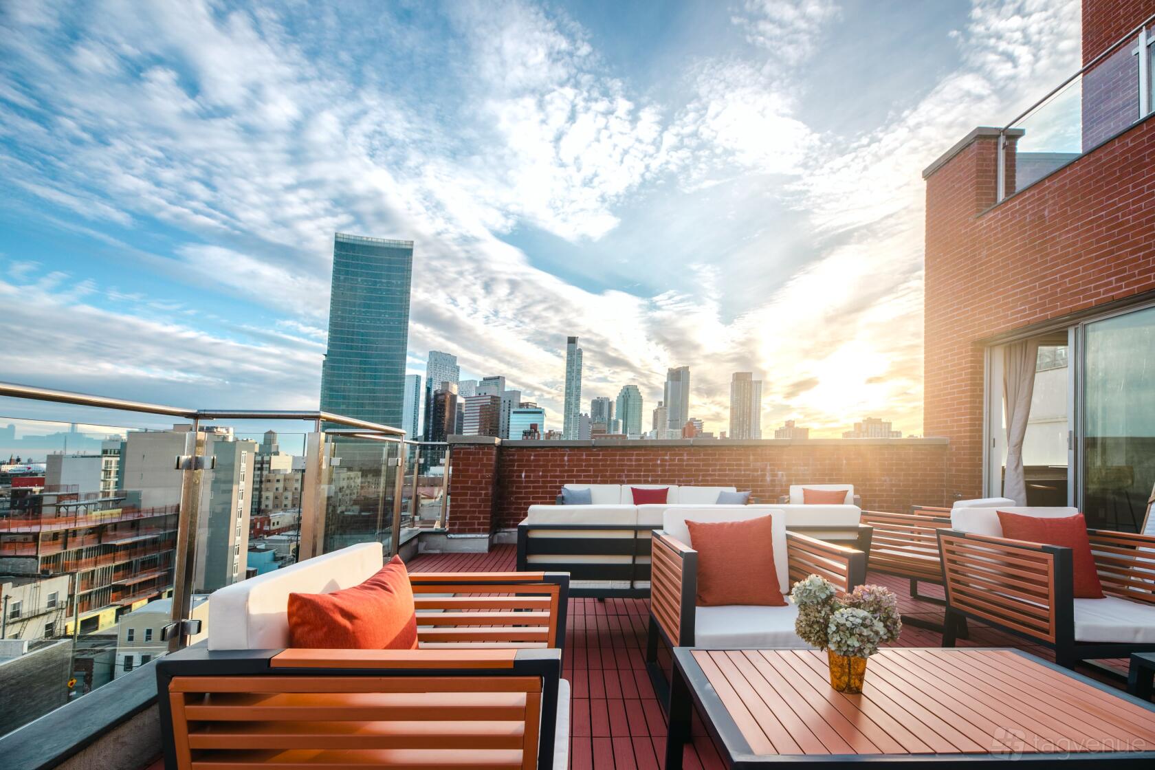 A rooftop lounge with cushioned seating, red accent pillows, glass railings, and city skyline views at The Modernist Hotel.