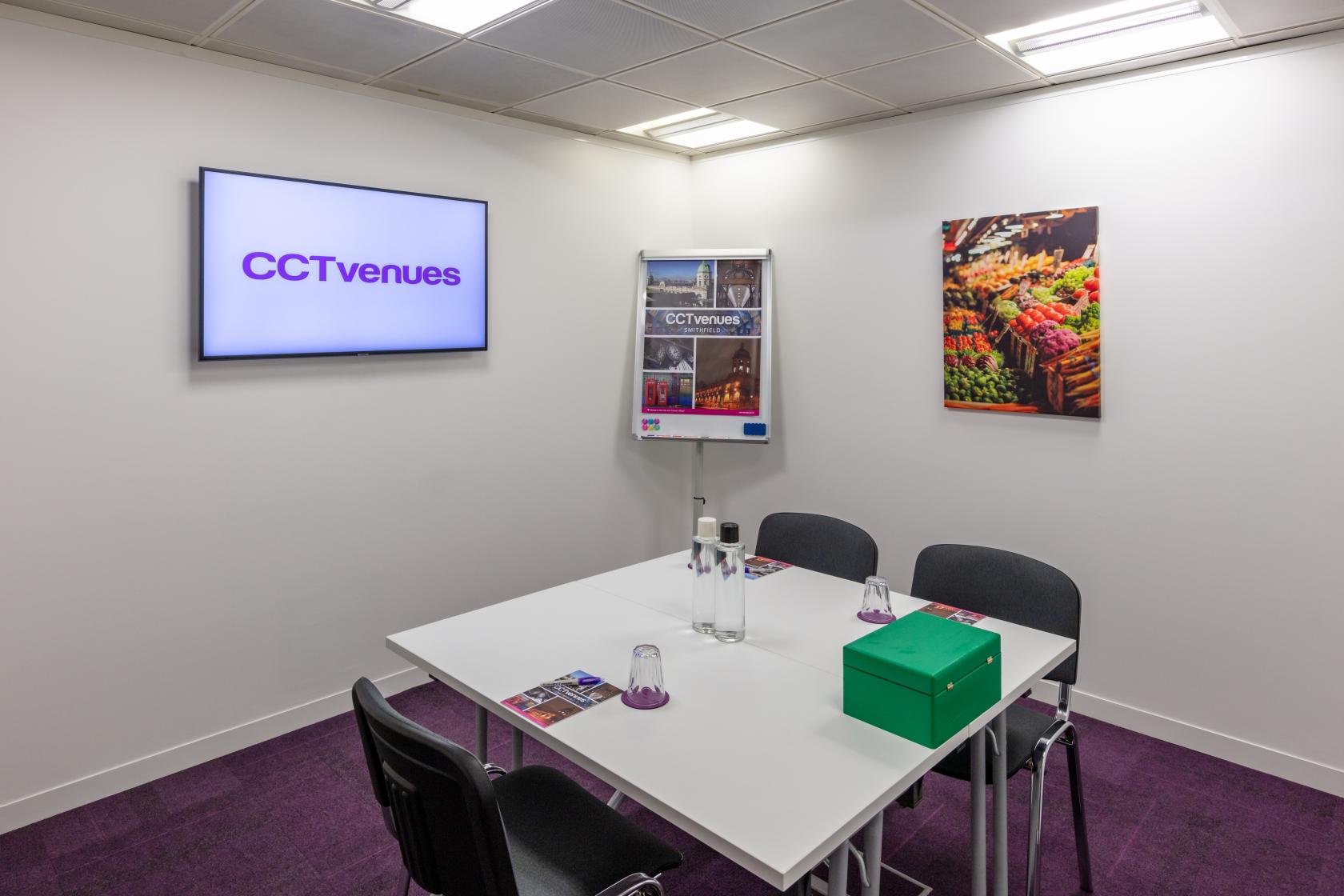 A meeting room with a white table, four chairs, wall-mounted screen, and bright artwork at CCT Venues - Smithfield.
