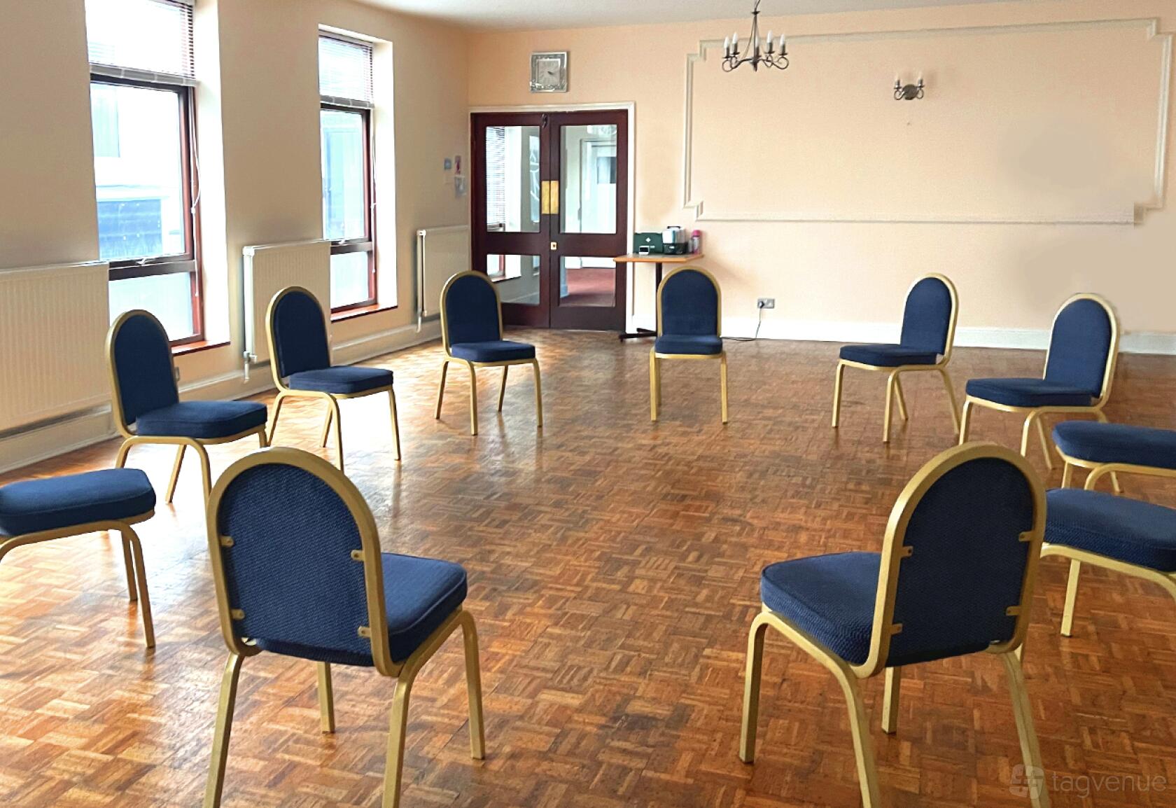 An event space with parquet flooring, large windows, and blue cushioned chairs arranged in a circle at The Rock Event Space, Walthamstow.