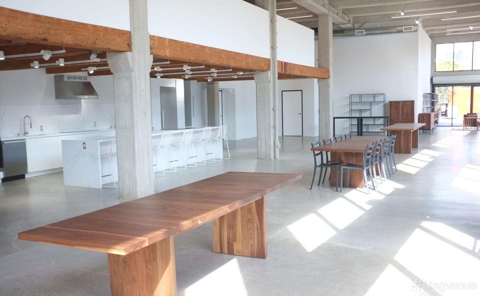 A restaurant with large wooden tables, open kitchen, concrete floors, and floor-to-ceiling windows at Feedfeed.