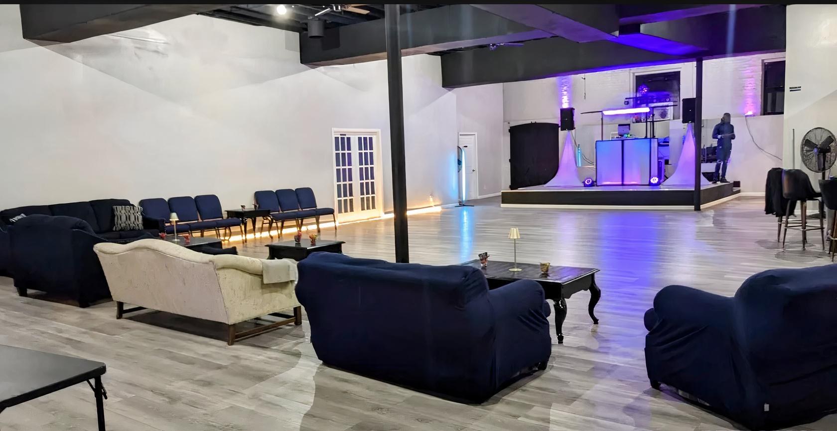 An event venue with a wood dance floor, lounge seating, and a DJ booth on stage at Ritmo Room.