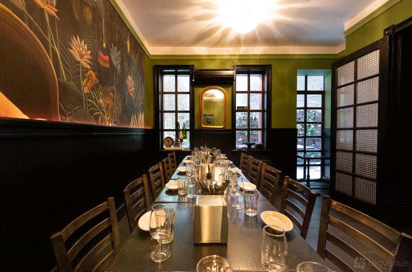 A dining room with a long table, dark wood chairs, jungle mural, and green walls at The Ten Bells.