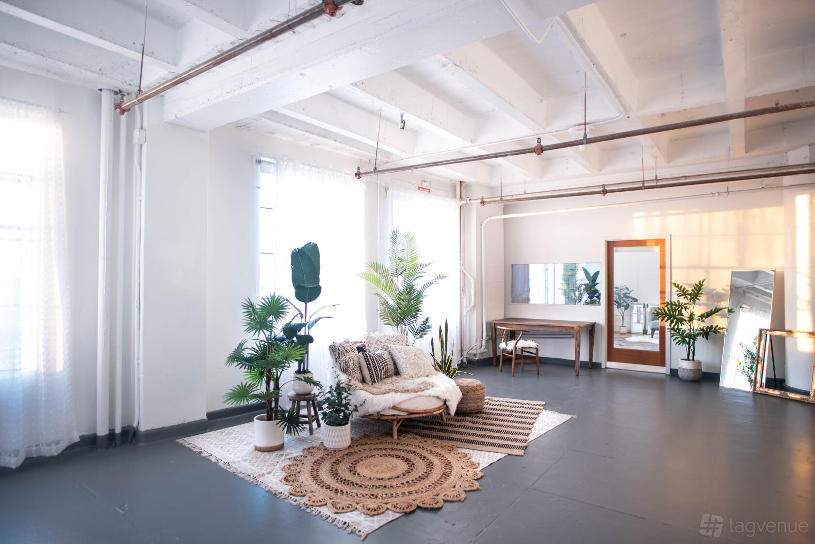An event venue with white exposed beams, large windows, and a seating area with plants and rugs at Skyline Boho.