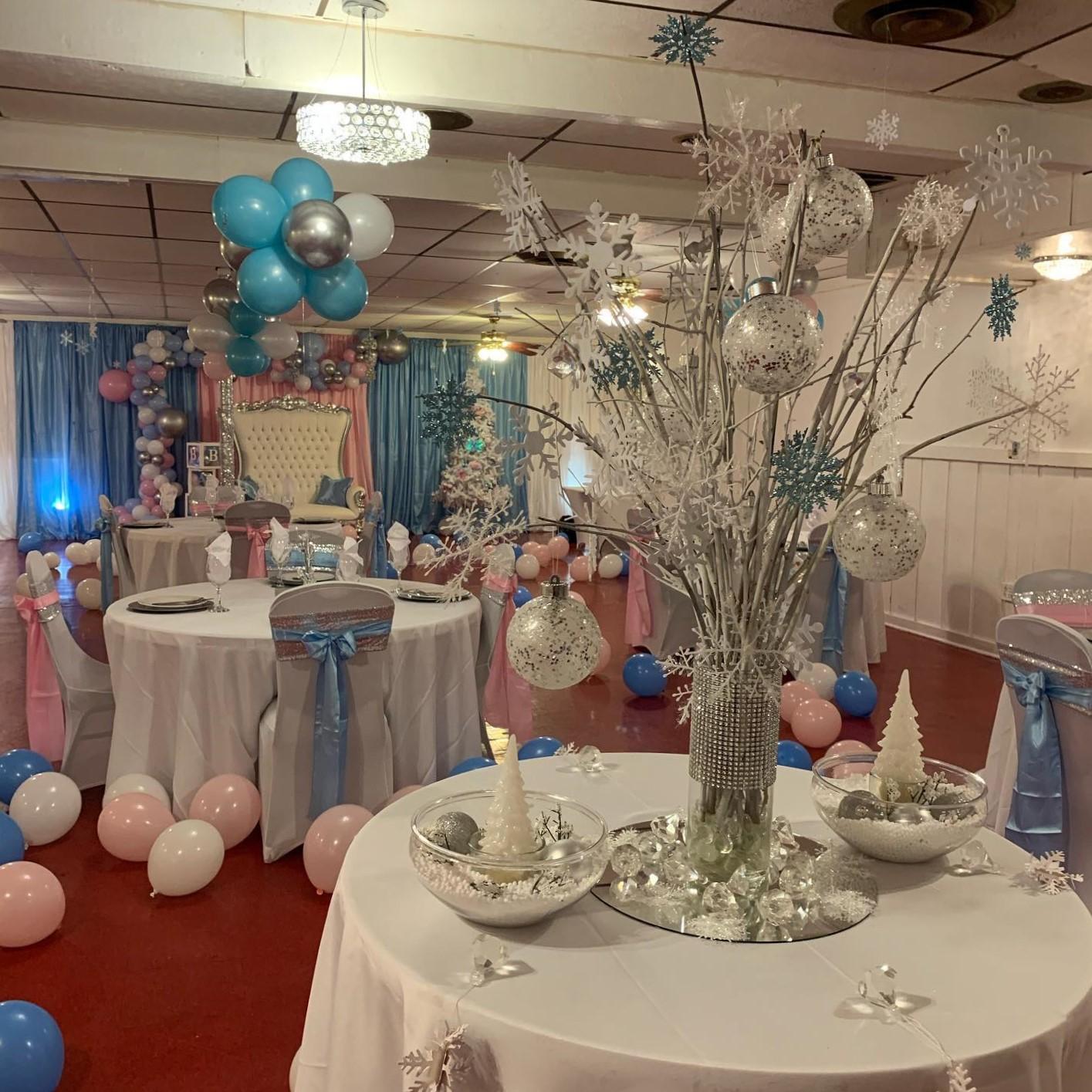 A banquet hall with round tables, silver and blue decorations, and balloon arrangements at Chuck’s Haven Banquet Hall.