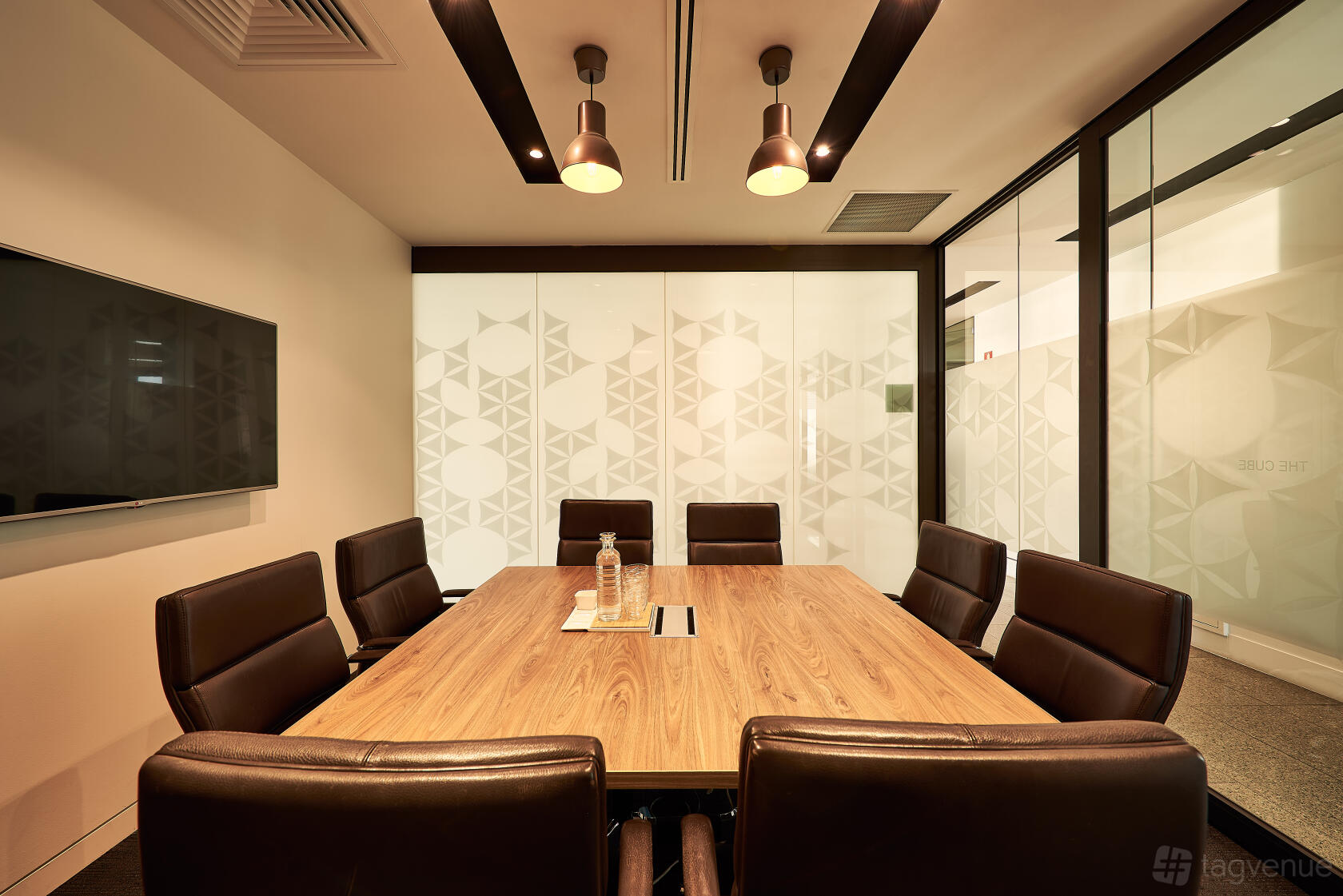 A meeting room with a wooden conference table, leather chairs, frosted glass walls, and pendant lighting at The Cluster.