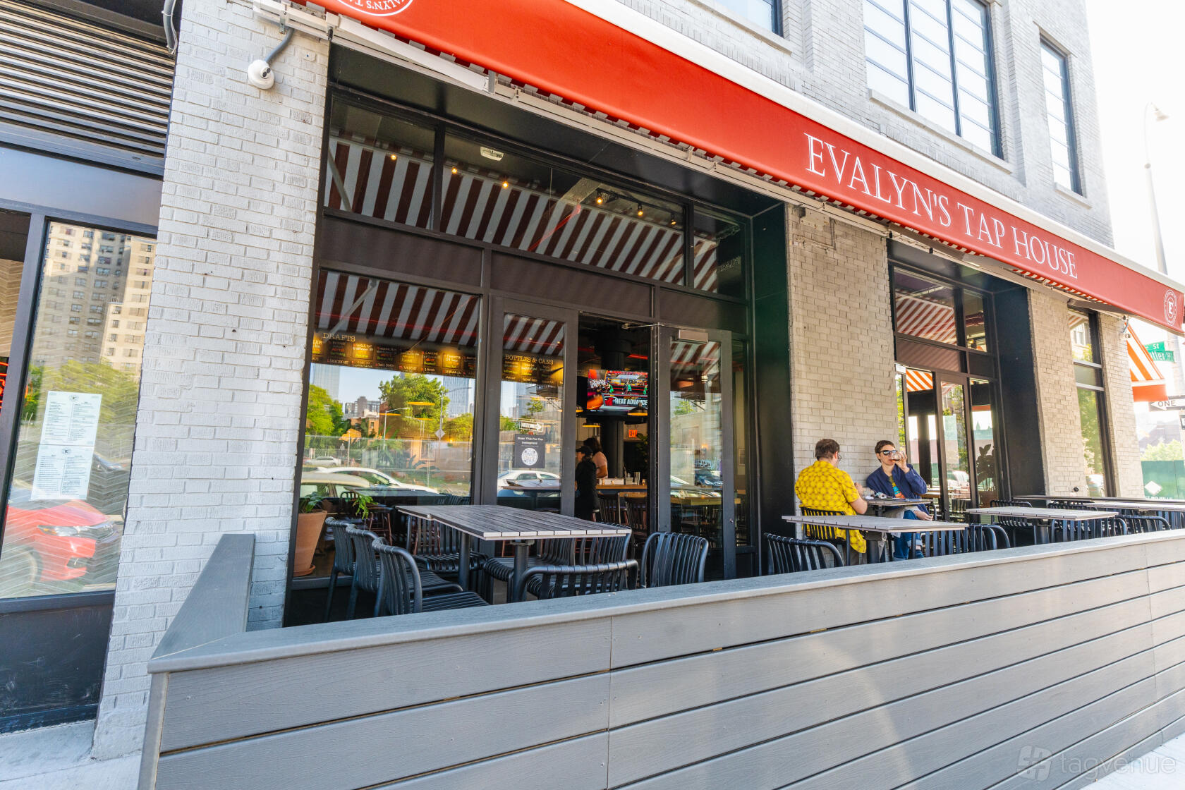 An outdoor deck with striped awnings, black chairs, and red umbrellas at Evalyns Tap House.