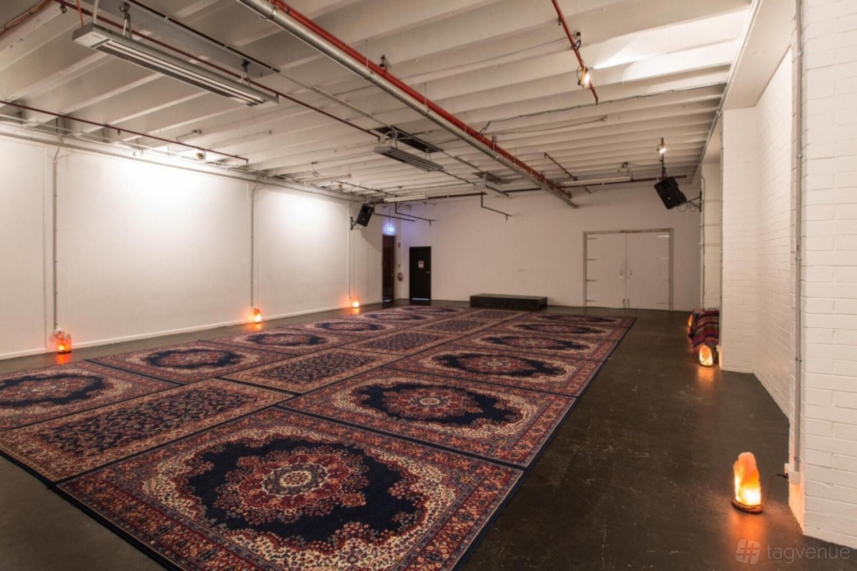 An event venue with exposed beams, ornate patterned rugs, and ambient floor lighting at Second Story Studios Engine Room.
