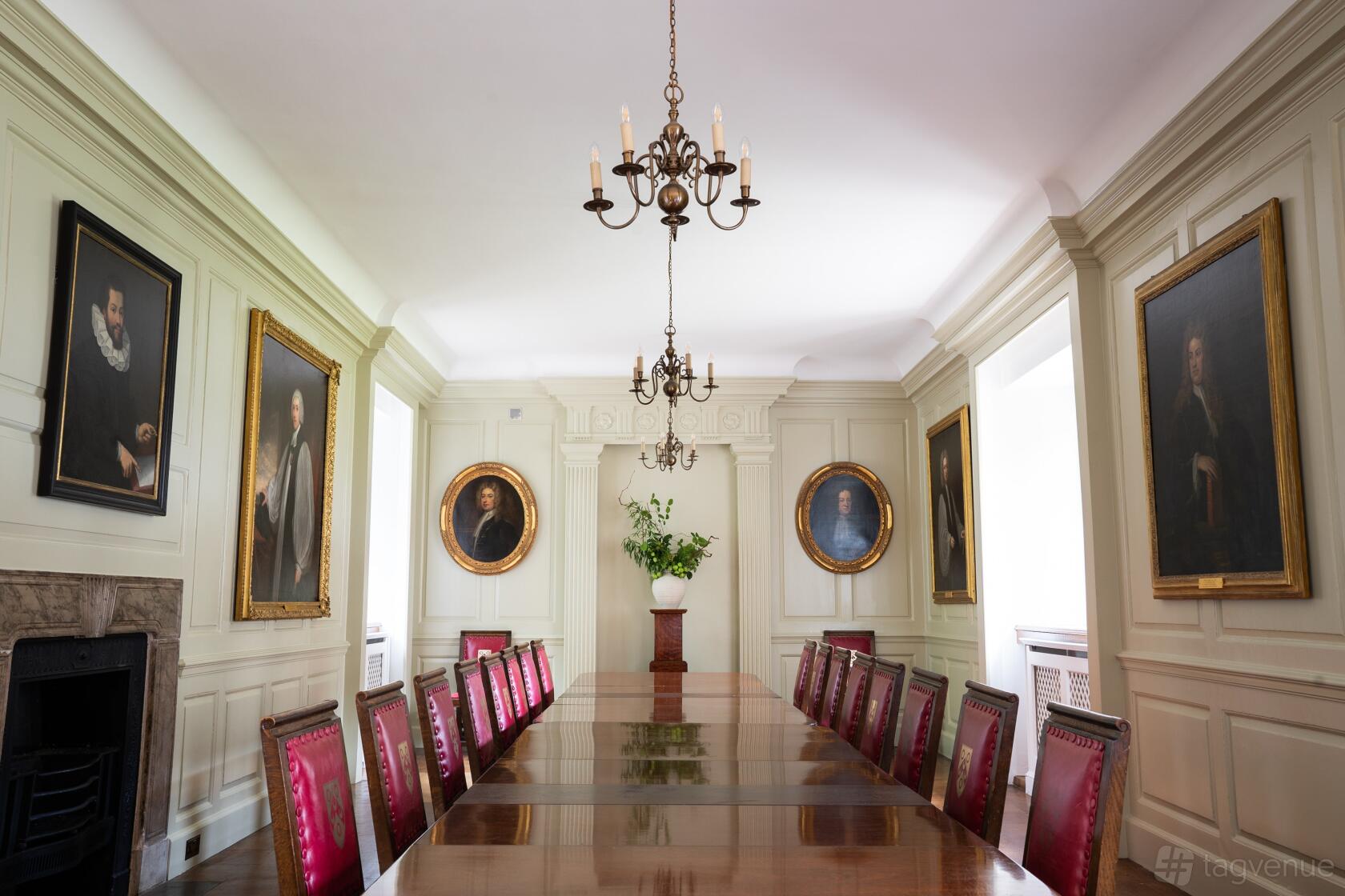 A historic hall with a long polished table, red leather chairs, chandeliers, and portrait paintings at The Charterhouse.