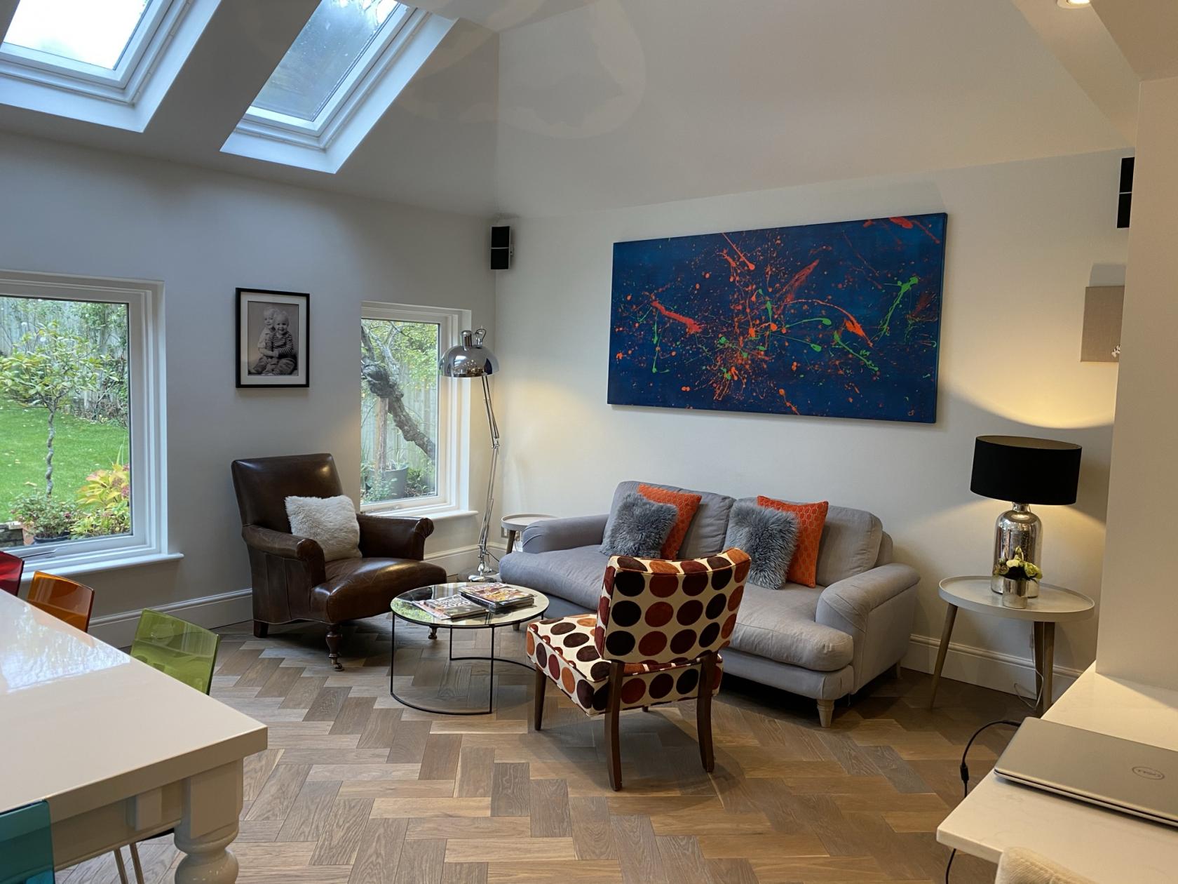 A house living area with skylights, herringbone wood floors, modern art, and large windows at Combemartin Road London SW18.