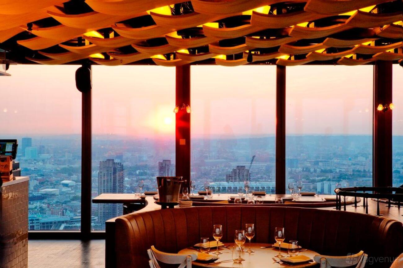 A restaurant with floor-to-ceiling windows, sunset city skyline views, and set dining tables at Duck and Waffle.