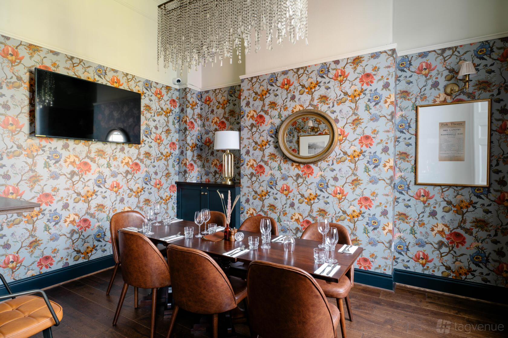 A dining room with floral wallpaper, a chandelier, and a set table with brown leather chairs at The Lillie Langtry.