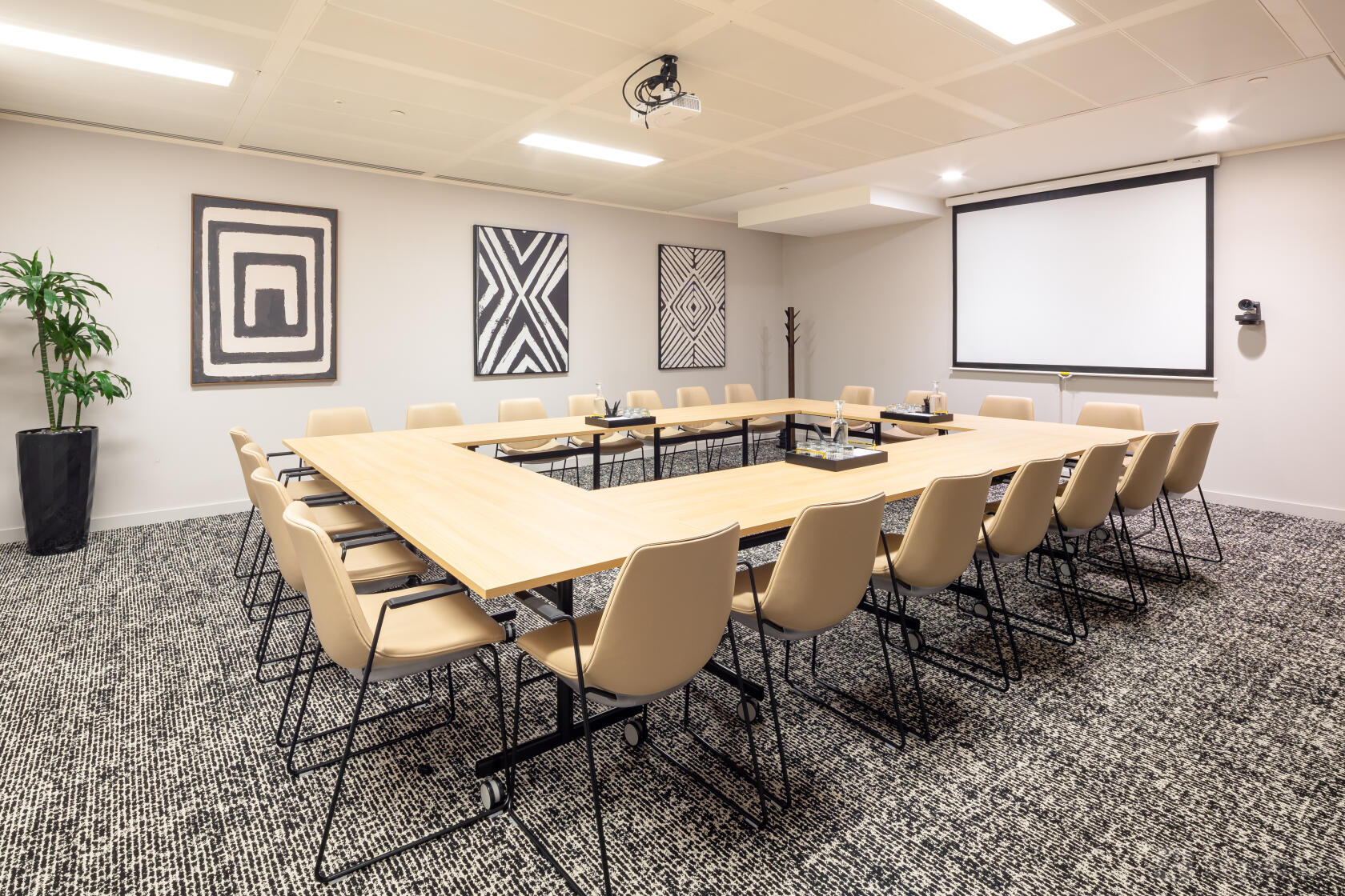 A meeting room with a U-shaped table setup, beige chairs, wall art, projector, and large screen at Landmark: 99 Bishopsgate, London.