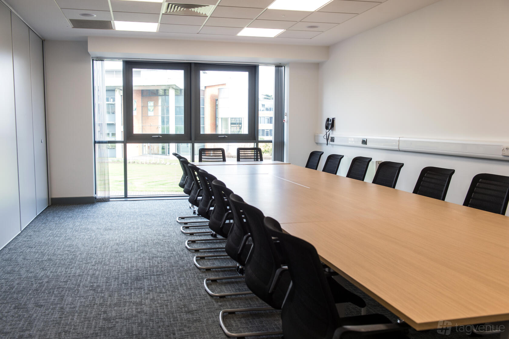A conference centre meeting room with a long boardroom table, black chairs, and floor-to-ceiling windows at Rothamsted Conference Centre.