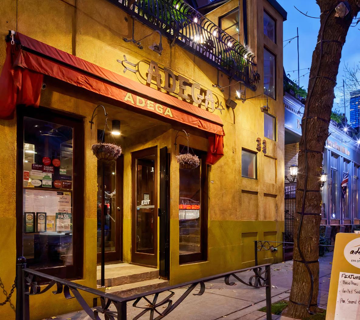 A restaurant with a red awning, warm yellow exterior, and entrance at Adega.