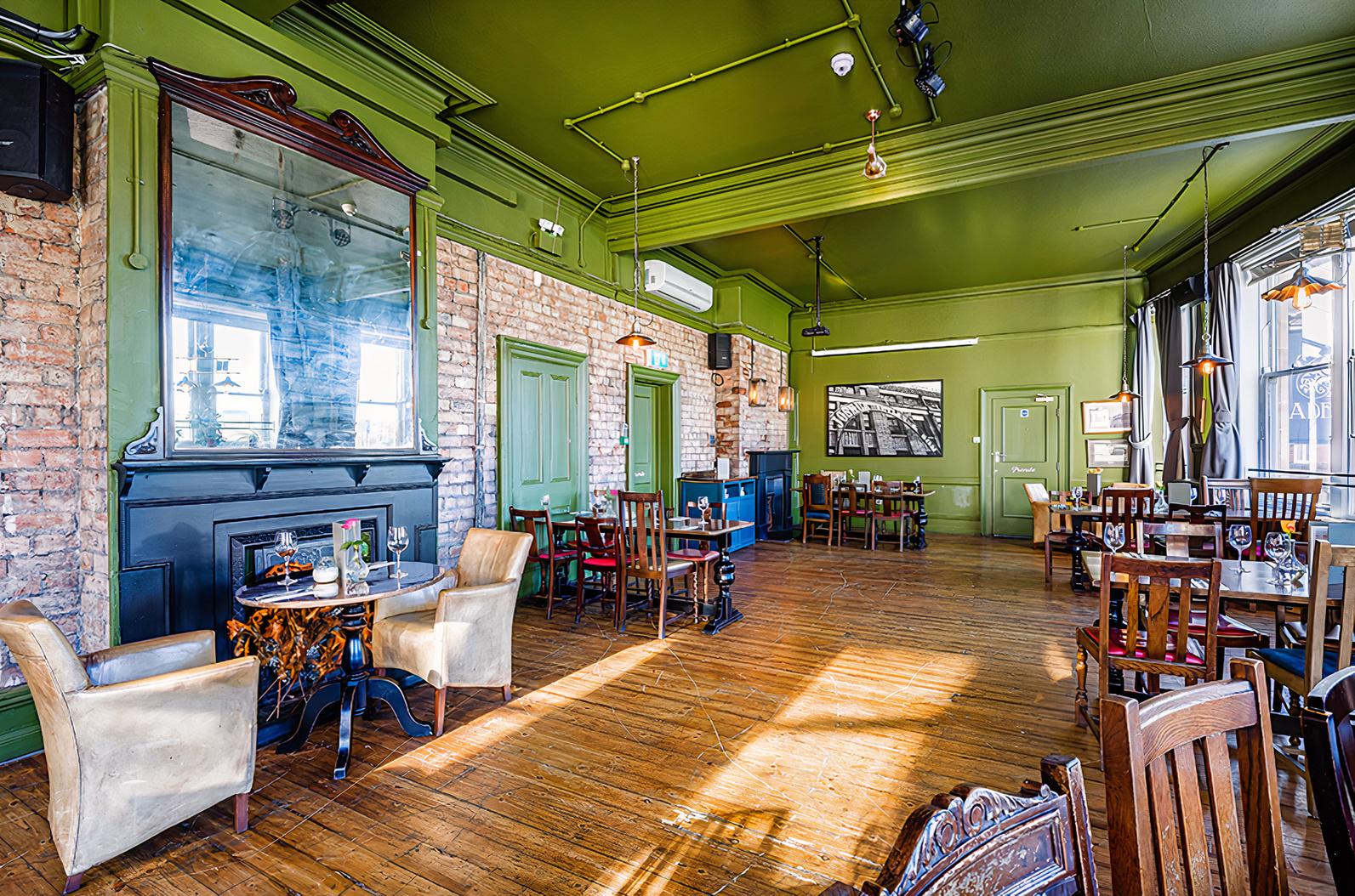 A dining room with exposed brick walls, wooden floors, and mismatched wooden chairs at The Adelphi Pub & Restaurant.