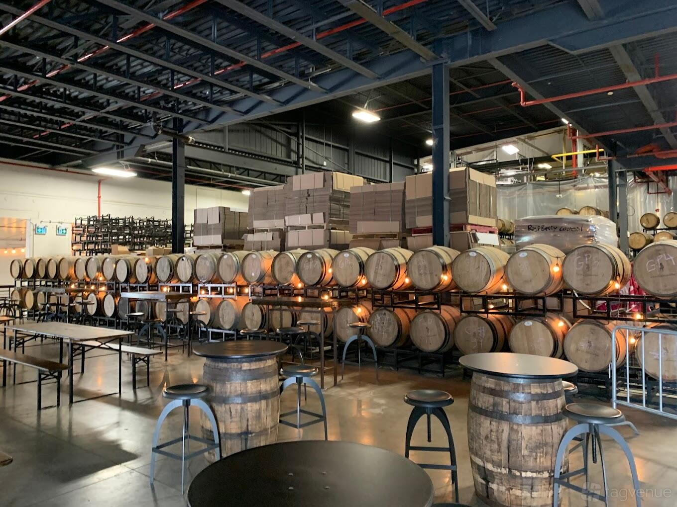 An event space inside a brewery with wooden barrels lining the walls and high-top barrel tables at Collective Ash Brewing.