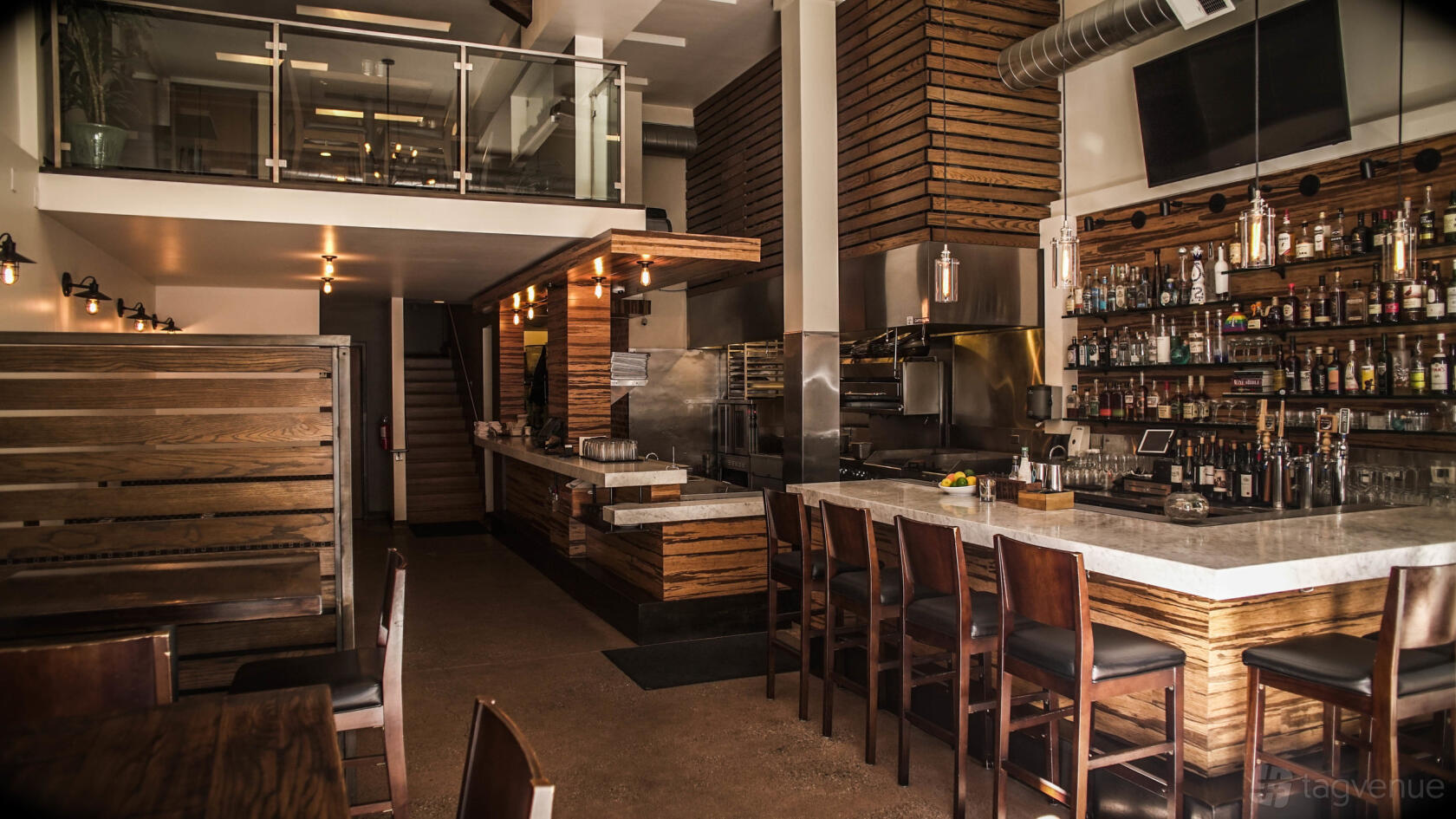 A restaurant with a marble bar, open kitchen, wood accents, and shelves of spirits at Aliment.