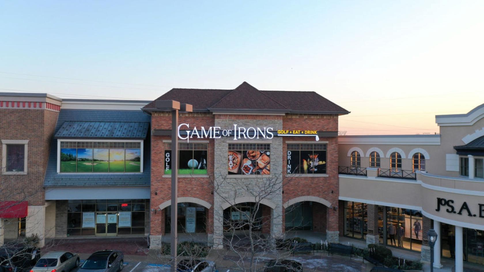 A golf club with a brick exterior and illuminated signage above large display windows at Game of Irons.