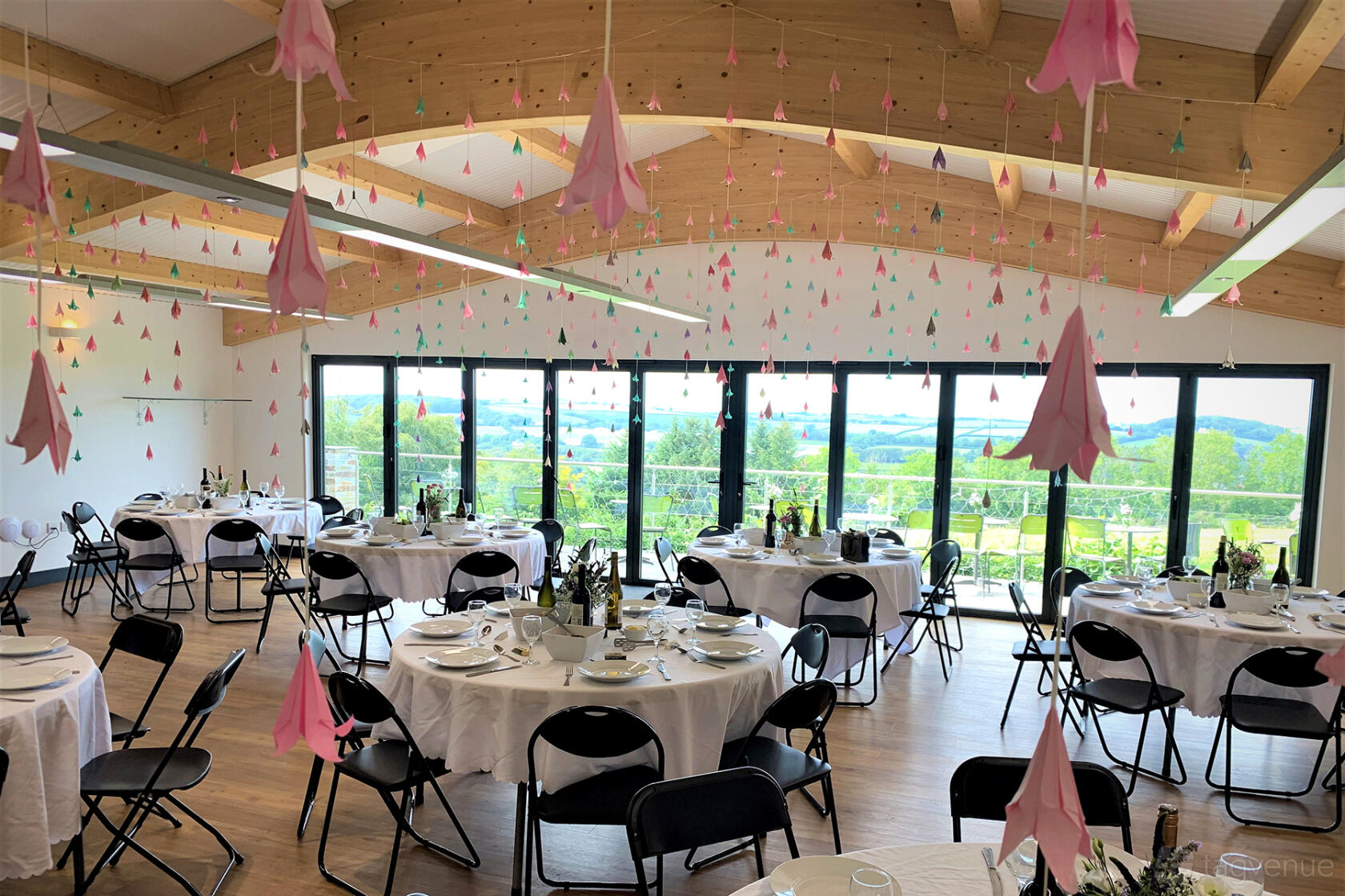 A function room with round tables set with white linens, black chairs, and floor-to-ceiling windows at Bracken Tor Weddings.