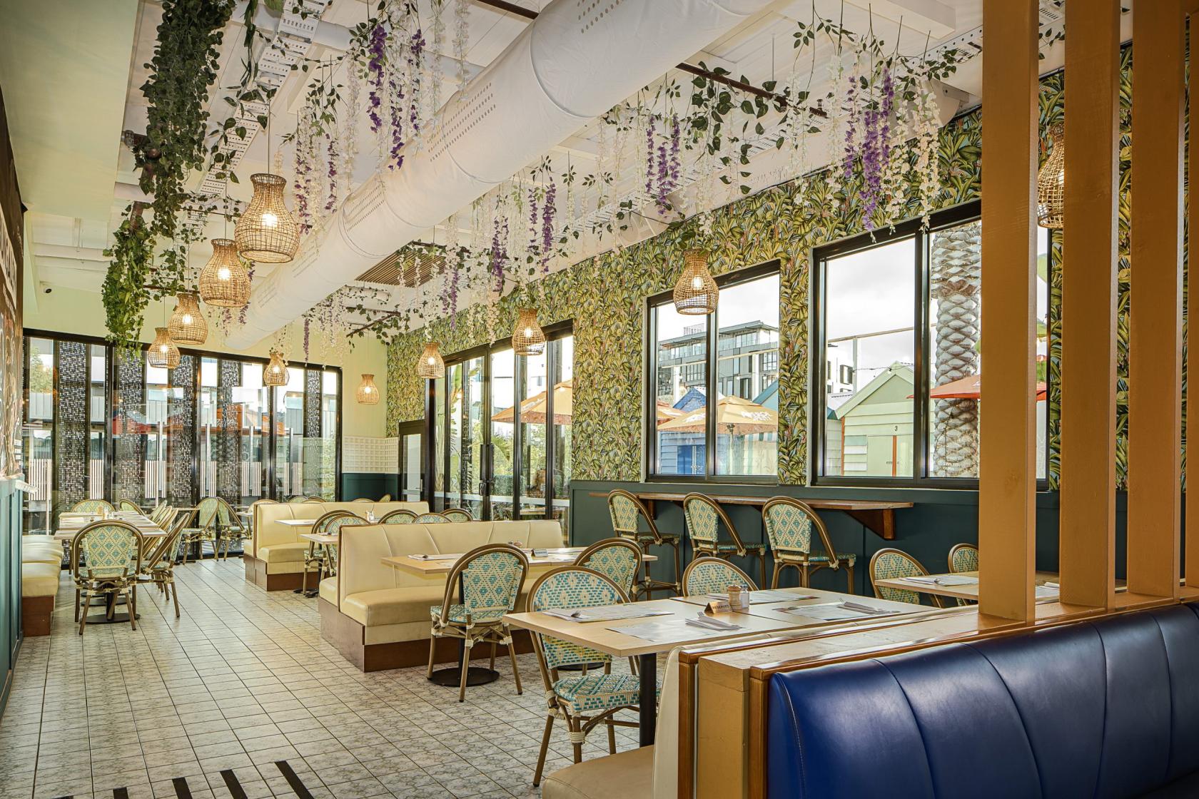 A dining room with hanging plants, rattan chandeliers, and light-colored booth seating at The Bungalow Beer Garden.