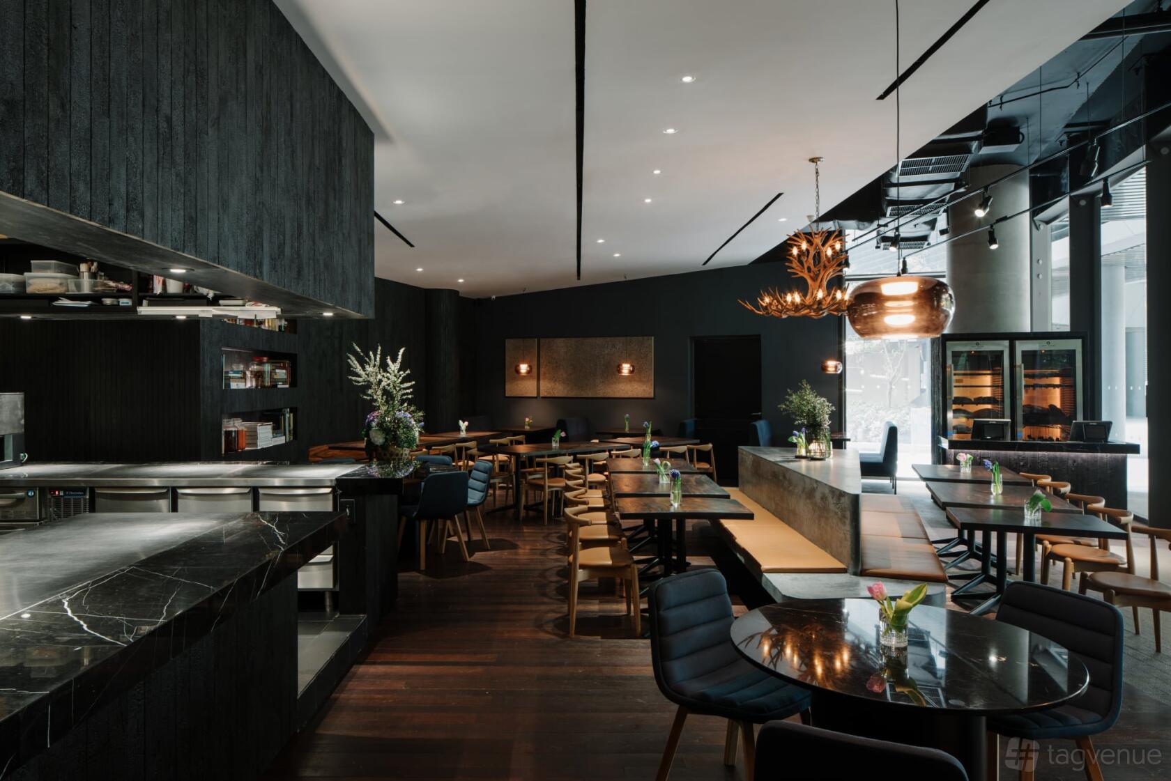 A restaurant with dark wood accents, open kitchen, pendant lighting, and mixed seating at NUDE Grill.