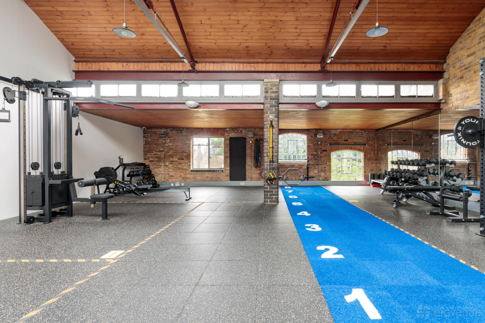 A fitness studio with exposed brick walls, large windows, gym equipment, and a blue sprint track at Fitness Workspace.
