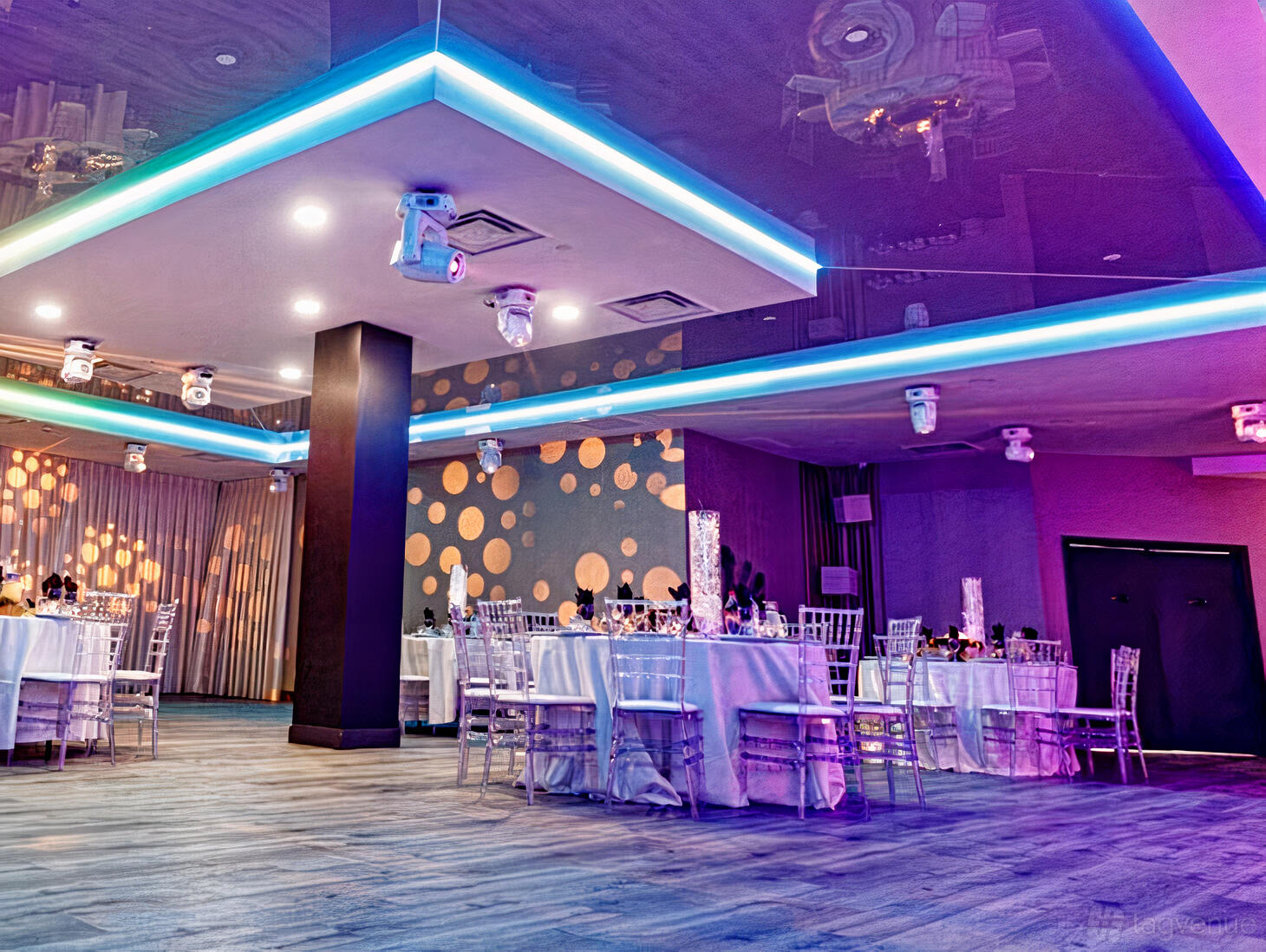 A hall with LED ceiling lights, patterned accent wall, and round tables with silver chairs at Fantasia Event Hall.