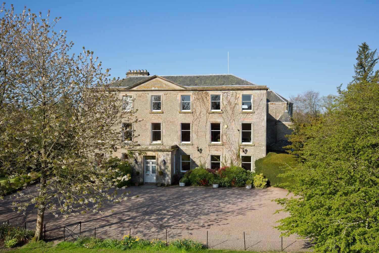 A country house with a grand stone facade, large windows, and gravel driveway at Kippilaw House.