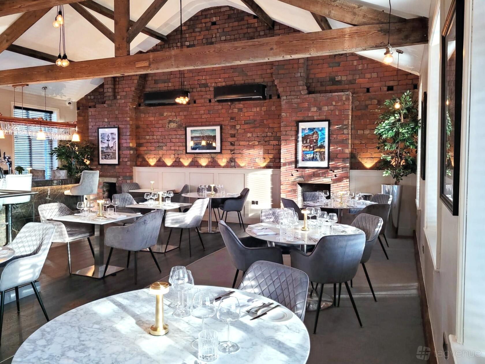 A restaurant with exposed brick walls, vaulted wooden beams, and round tables set for dining at Heaney & Mill.