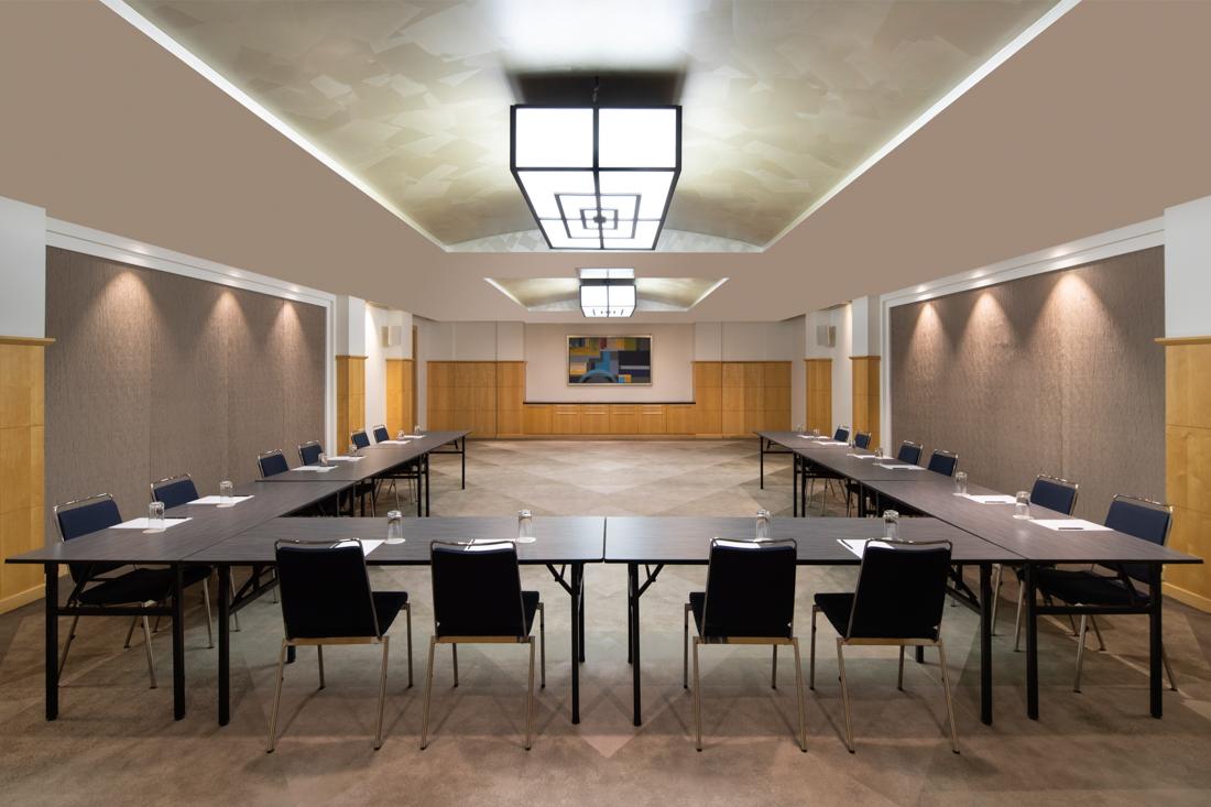A meeting room with U-shaped black tables, cushioned chairs, and large geometric ceiling lights at Swissotel Sydney Maple Room.