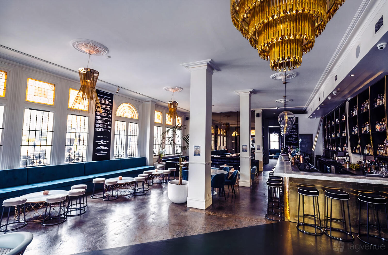 A cocktail bar with velvet banquette seating, gold chandeliers, and a long mirrored bar at The Kilburn.