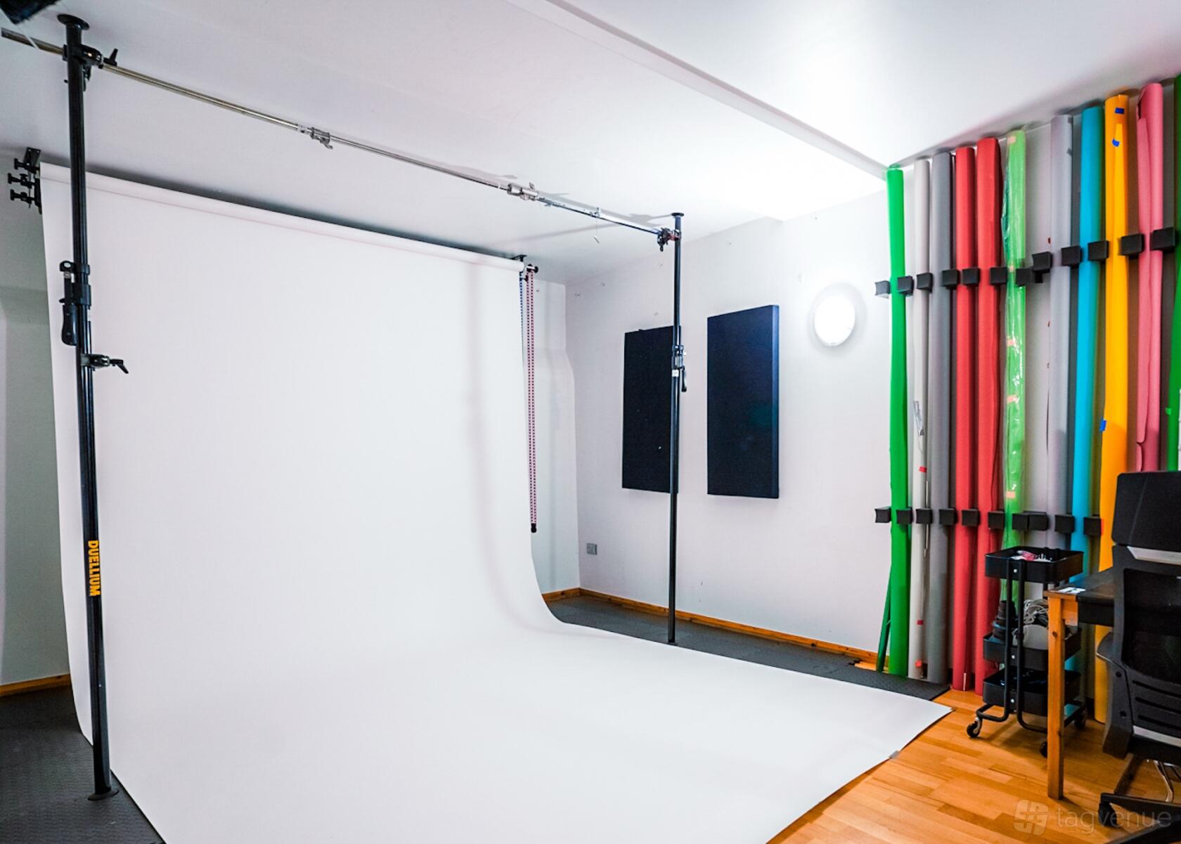 A photo studio with a white cyclorama backdrop, colored paper rolls, and wood flooring at Colores - London photo studio.