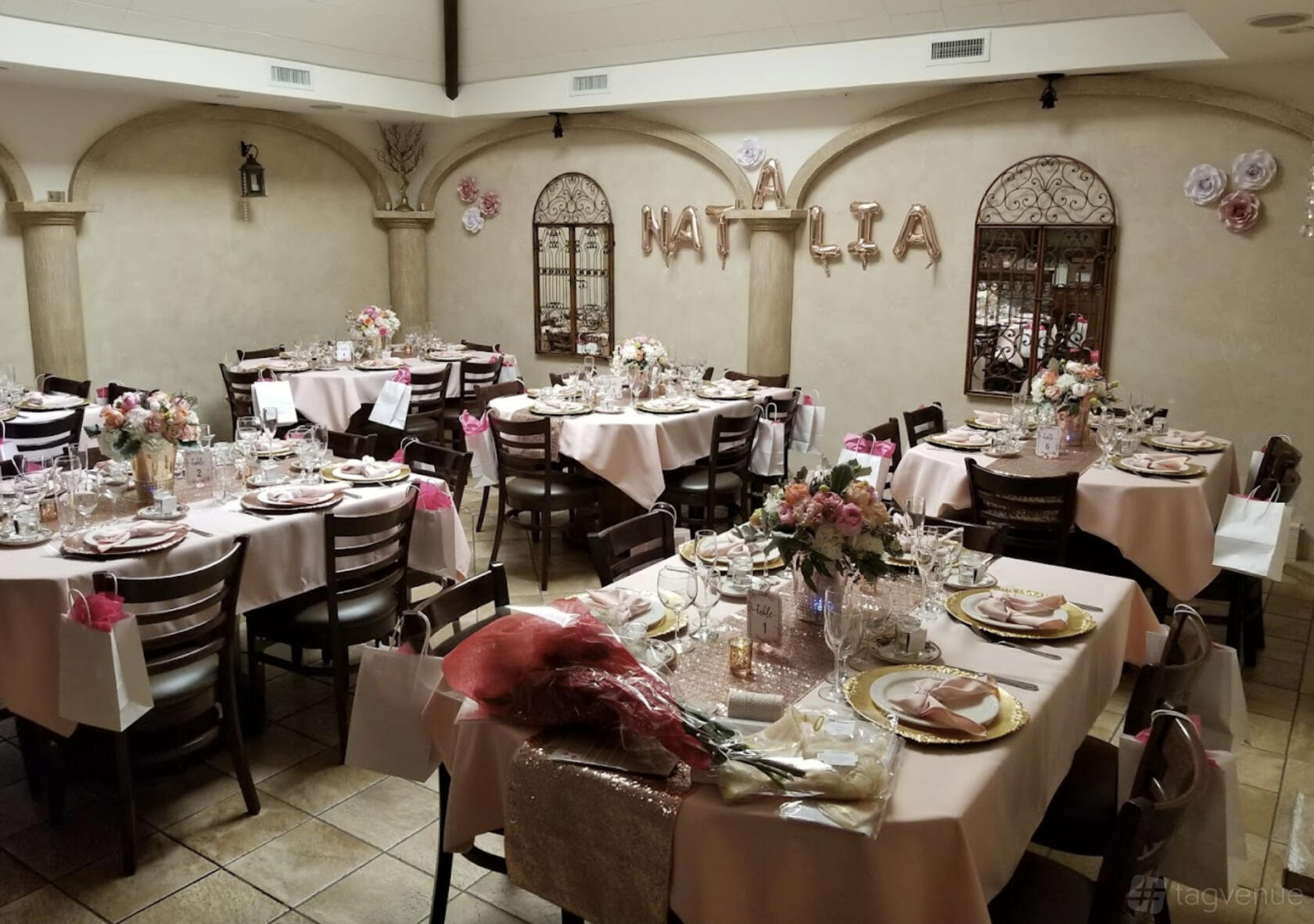 A restaurant event room with round tables dressed in white linens, floral centerpieces, and gold chargers at La Locanda.