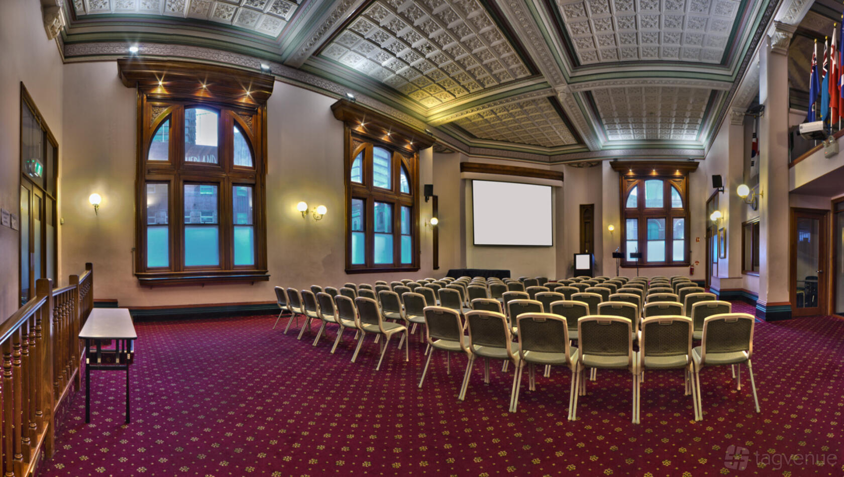 A conference hall with arched windows, ornate ceiling panels, and rows of chairs facing projection screens at Embassy Conference Centre.