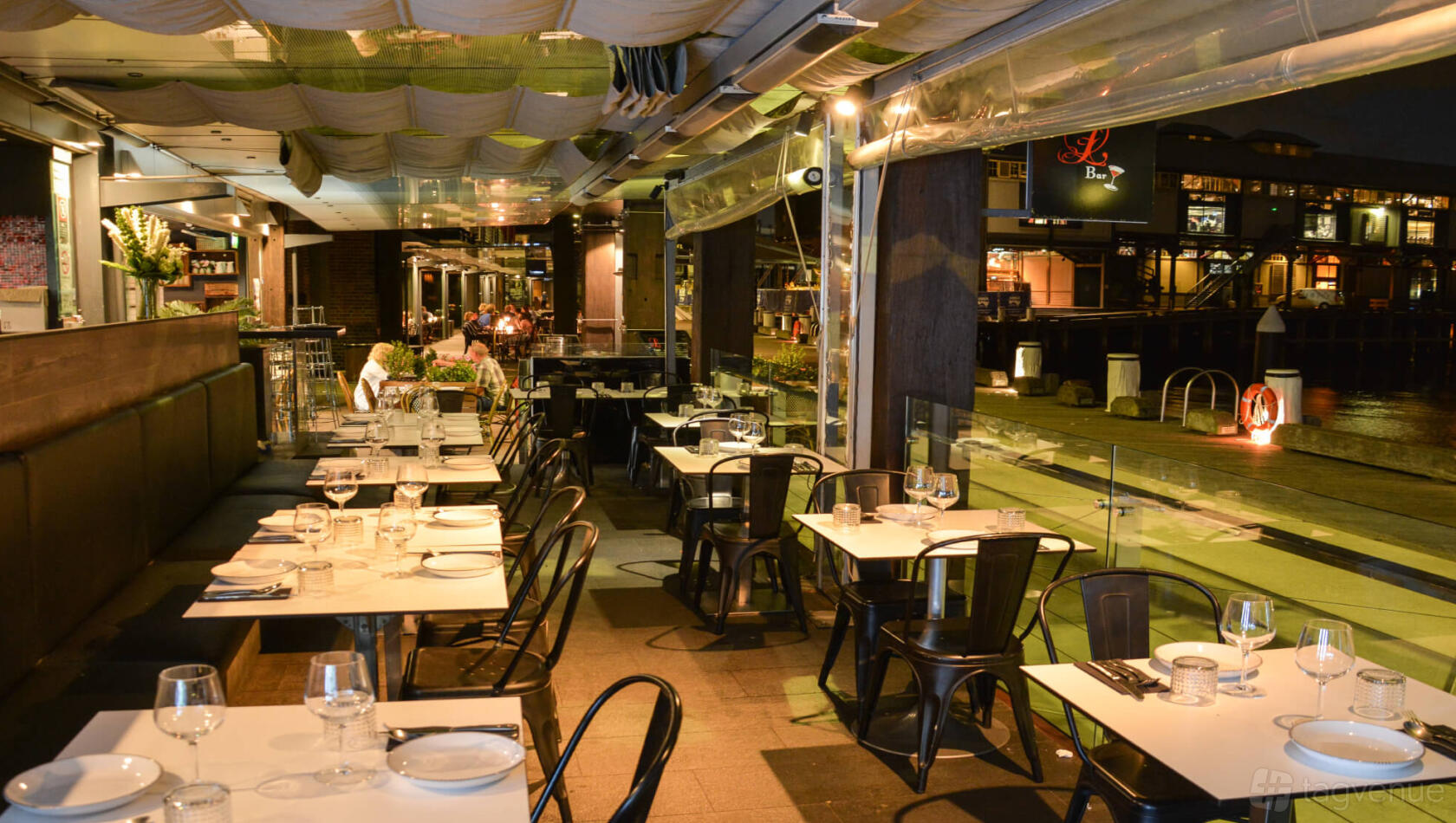 A restaurant with waterfront outdoor seating, black chairs, and tables set with glassware at Lavana Restaurant.