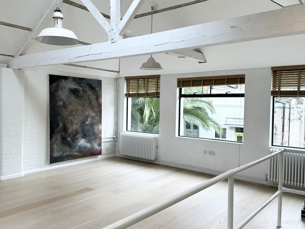 A yoga studio with light wood floors, white brick walls, large windows, and exposed beams at Sound Temple Studio.