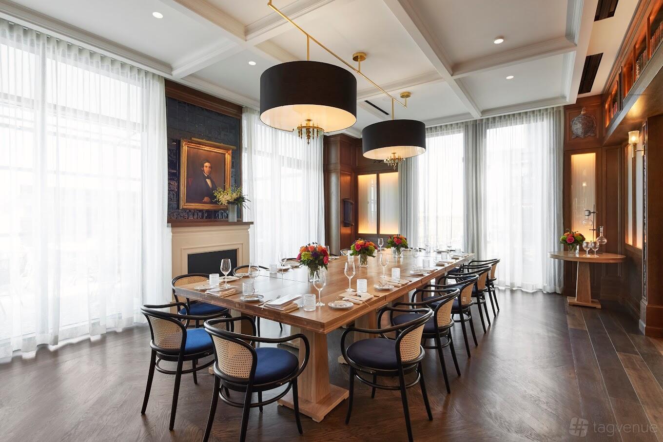A dining room with a long wooden table, cane-back chairs, large black pendant lamps, and floor-to-ceiling windows at Del Mar.