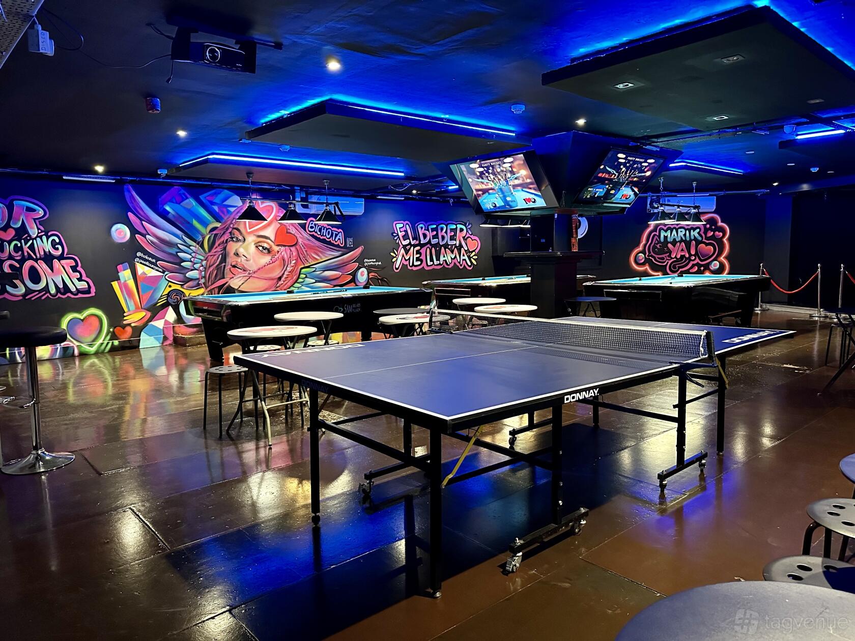 A bar with a central ping pong table, stools, and colorful graffiti murals at Bola 8.
