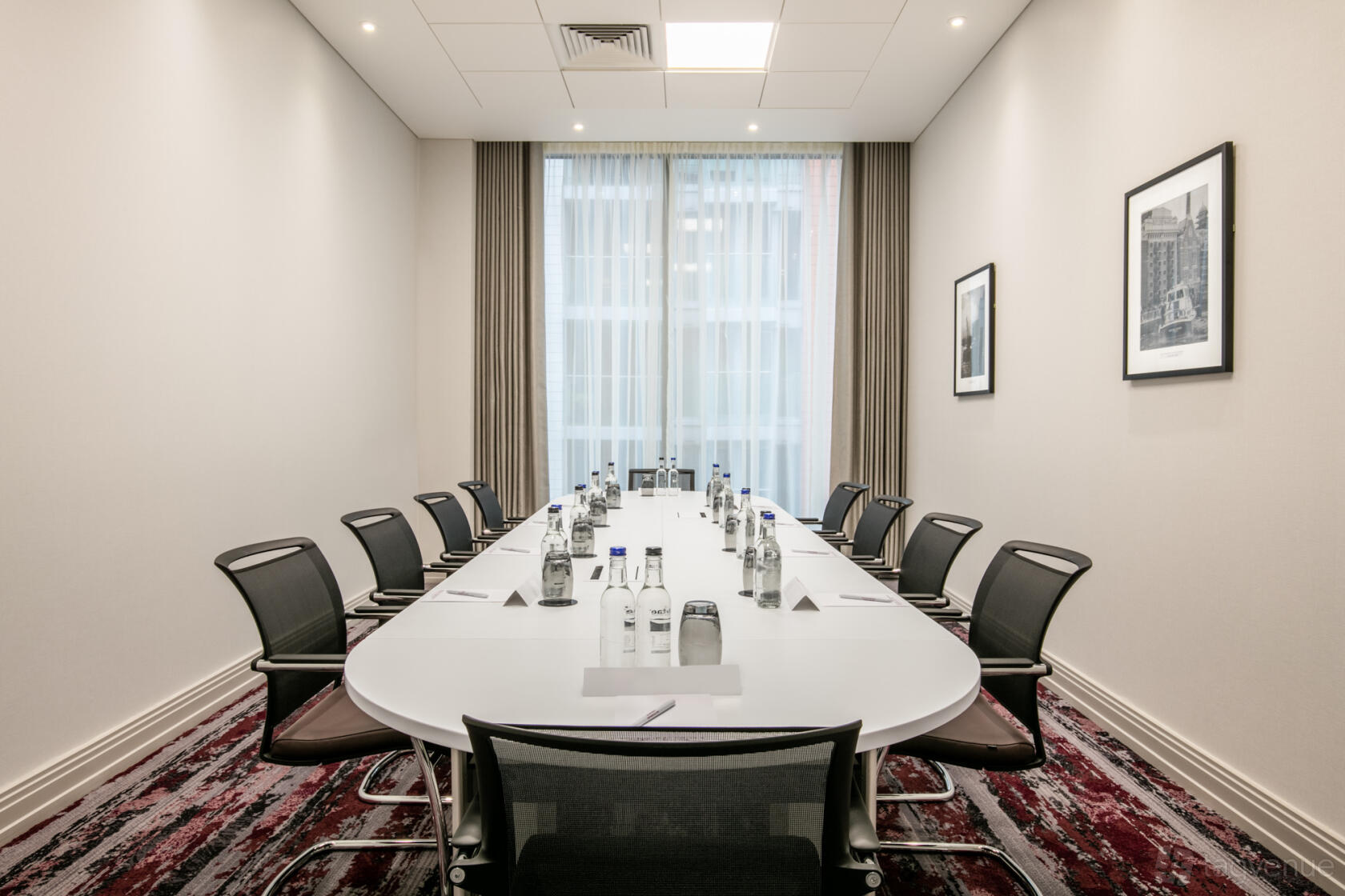 A hotel meeting room with a long boardroom table, black chairs, bottled water, and floor-to-ceiling windows at Crowne Plaza London Docklands.