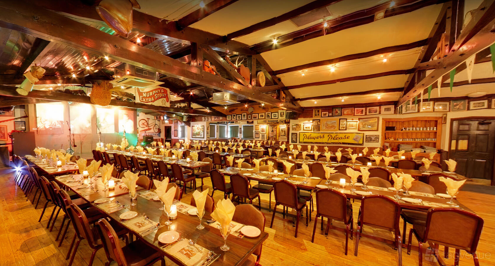 An event space in a pub with long banquet tables, wooden beams, framed artwork, and warm lighting at The Merry Ploughboy Pub.