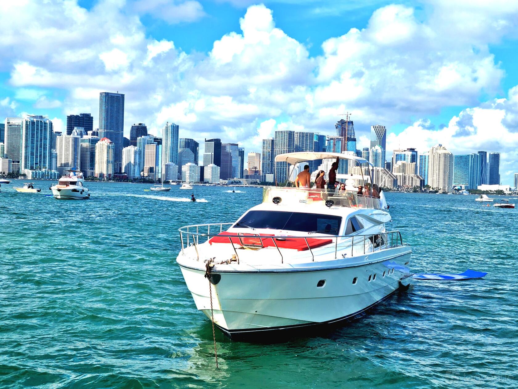 A boat with an upper deck lounge and a red sunbed anchored on the water with city skyline views at Boat Charters.